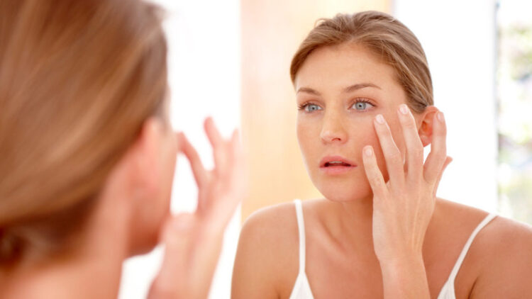 A naturally gorgeous woman applying moisturizing cream in a mirror